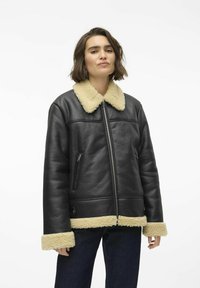 Veste en cuir noir avec un col et des poignets en fausse fourrure crème, dotée d'une fermeture éclair à l'avant et de poches latérales. Texture lisse avec une coupe structurée.