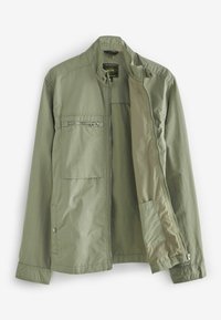 Veste légère olive avec col montant, fermetures éclair et pressions, plusieurs poches et texture lisse.