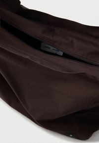 Smeđa platnena torba sa zatvaračem, koja ima glatku teksturu i vidljivu oznaku branda unutar. Jednostavni dizajn bez dodatnih akcenata.