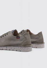 Zapatos de cuero gris claro con cordones verdes, texturizados, de perfil bajo, que presentan una suela blanca moteada y un sutil logo en el lateral.