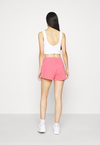 Vit ärmlös crop top, ljusrosa shorts, avslappnad passform, enfärgad textur, bakvy, bärs med vita sneakers och sockor.