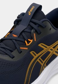 Tenger�észkék futócipő hálós felsőrésszel, narancssárga részletekkel és fehér talppal. Jellemzői a lekerekített orr és a kontrasztos cipőfűzők.