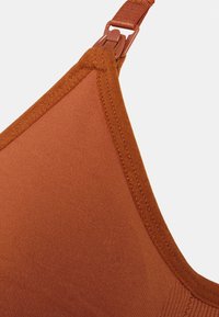 Sutiã de cor ferrugem com tecido liso e estriado, alças ajustáveis e design elegante. Apresenta costuras reforçadas nas bordas para maior durabilidade.