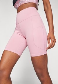 Różowe spodenki sportowe wykonane z elastycznego materiału, z wysokim stanem, boczną kieszenią i gładką fakturą z minimalnymi detalami szwów.