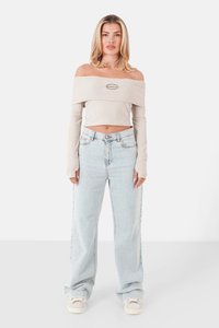 Beige, schulterfreies, geripptes Crop-Top mit langen Ärmeln; kombiniert mit hellblauen, hoch taillierten, weiten Jeans; weiße Sneakers.