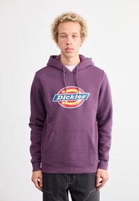 Violetinės spalvos medvilnės mišinio džemperis su priekine kišene ir apvaliu logotipu, kuriame rašoma "Dickies" mėlyna ir raudona spalvomis.