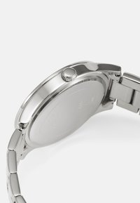 Srebrni sat od nehrđajućeg čelika s glatkim okruglim kućištem, krunicom i poliranim narukvicom od poveznica. Prikaz stražnje strane, pokazuje čist završetak.