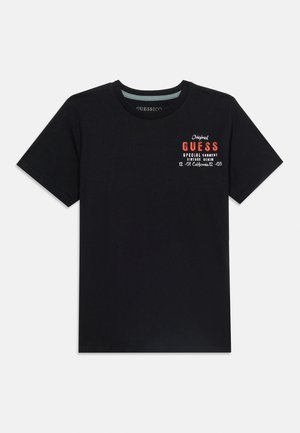 Maglietta nera a maniche corte con scollo a girocollo, piccolo testo "GUESS" rosso e bianco e stampa in denim vintage sul petto sinistro.