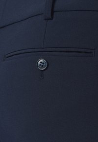 Granatowe spodnie garniturowe o eleganckim kroju, gładkiej fakturze materiału, z tylną kieszenią zapinaną na guzik oraz subtelnymi detalami przeszycia.