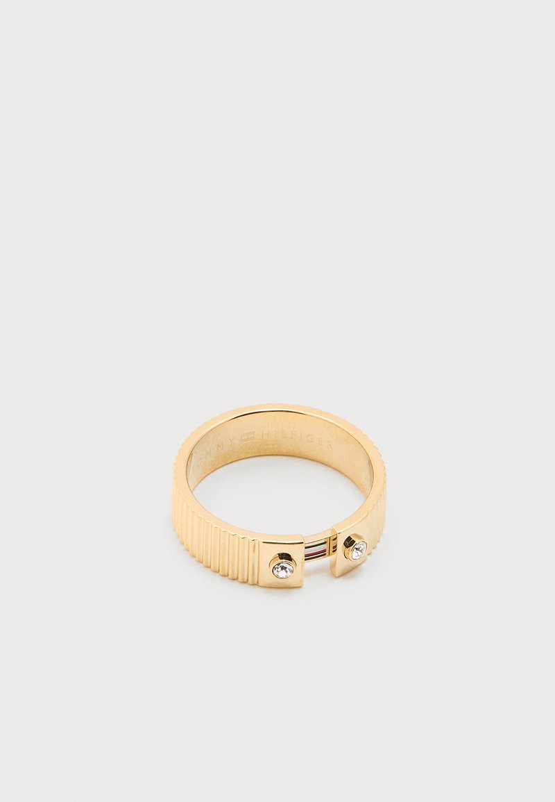 Δαχτυλίδι σε χρυσαφί απόχρωση με ραβδωτό σχέδιο, δύο μικρές διάφανες πέτρες και χαραγμένο το λογότυπο Tommy Hilfiger στο εσωτερικό της μπάντας.