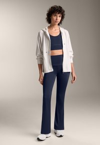 Granatowy komplet sportowy składający się z dopasowanego crop topu i spodni legginsów z wysokim stanem, w połączeniu z jasnoszarym rozpinanym kapturem i białymi sneakerami.