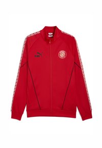 Rød zip-up jakke lavet af glat stof, med sorte accenter, logo på brystet og mønstrede side-striber. Lange ærmer og høj krave.