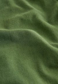 Olivově zelená látka s hladkým, mírně texturovaným povrchem a jemným diagonálním tkaním. Materiál vypadá jemně a pružně.