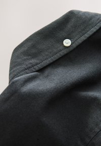 Zbliżenie na czarną tkaninę z widocznym przeszyciem i pojedynczym białym guzikiem przyszytym blisko krawędzi części ubrania.