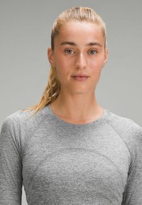 Grau langärmliges Sportoberteil mit strukturierter Oberfläche und Raglanärmeln, das eine dezente, gebogene Detailierung an der Brust aufweist.