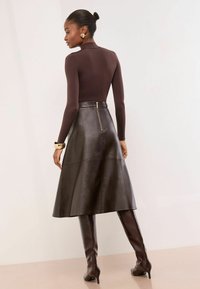 Barna, testhez simuló, hosszú ujjú felső, magas nyakkivágással, fekete bőr A-vonalú szoknyával párosítva, amely hátul zipzáros, és barna, térd fölé érő, stiletto csizmákkal.