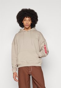 Felpa beige con tasca a marsupio frontale, coulisse e tasca con zip sulla manica con accento rosso. Tessuto morbido, vestibilità relax.