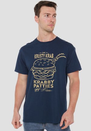 Navy blue cotton t-shirt featuring a graphic print of a burger and text "Krusty Krab Serving Krabby Patties Since 1999" in gold. Short sleeves.