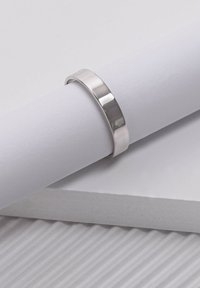 Gepolijste zilveren ring met een gladde, vlakke oppervlak en een lichte glans. Geplaatst op gestructureerd wit papier, waarmee het minimalistische ontwerp wordt benadrukt.