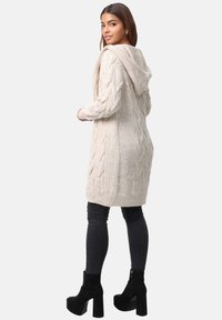 Beige kabelstickad cardigan med huva, med ribbad nederkant och texturerat mönster. Buren över svarta jeans och svarta klackstövlar.
