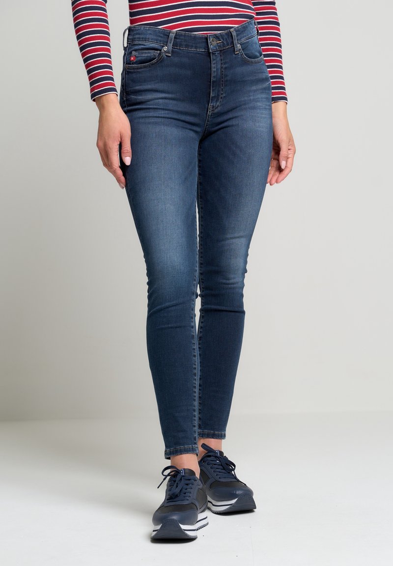 Tunna blå jeans i denim med midjestighöjd, fem fickor och en slät textur. Bärs tillsammans med mörka sportskor.