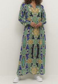 Abito maxi con motivo floreale multicolore, nelle tonalità di verde, giallo e blu; maniche lunghe, scollatura a V, abbinato a sneakers bianche.