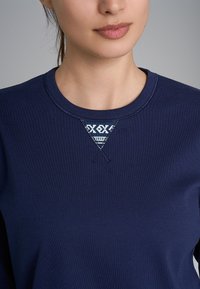 Felpa navy con scollo a girocollo, decorata con un motivo triangolare ricamato in bianco sul petto. Tessuto in cotone liscio, vestibilità casual.