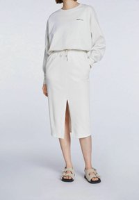 Sudadera blanca de manga larga y cuello redondo combinada con una falda blanca hasta la rodilla con una apertura en la parte delantera y cintura ajustable con cordón.