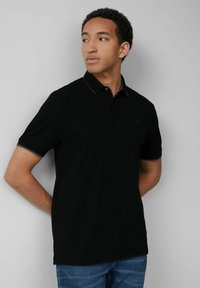 Schwarzes Polohemd mit Kragen und zwei Knöpfen, mit einem kontrastierenden Besatz. Hergestellt aus glattem Stoff, getragen mit Jeans.