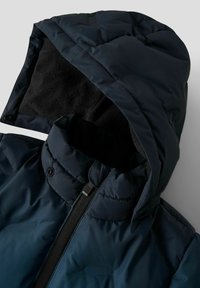 Marineblå puffjakke med avtagbar hette, som har fleecefôr, stikninger og en senter glidelås med en dragløkke.