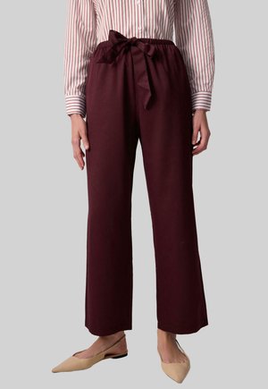 Burgundy wide-leg trousers with a fabric belt. Smooth texture and a relaxed fit, paired with a striped button-up shirt. Nude flats.