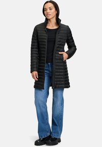 Sort puffet jakke med høj krave, der har vandret quiltet design, lynlåslukning foran og sidelommer; båret over blå jeans.