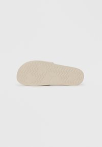 Light beige sneaker sole with a textured zigzag pattern and rounded edges. Features a prominent logo at the center. Smooth surface.