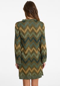 Knit dress with a zigzag pattern in shades of green, gold, and brown. Long sleeves and a simple round neckline. Textured fabric.