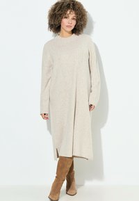 Abito lavorato a maglia beige con maniche lunghe, texture a coste, collo alto e spacchi laterali, abbinato a stivali beige al ginocchio.