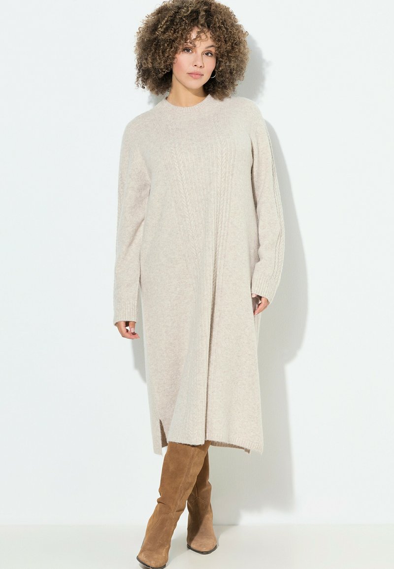 Abito lavorato a maglia beige con maniche lunghe, texture a coste, collo alto e spacchi laterali, abbinato a stivali beige al ginocchio.