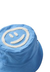 Sininen kangasateria hattu, jossa on päällä kirjailtu valkoinen teksturoitu hymyilevä kasvot. Pyöreä muoto leveällä reunuksella.