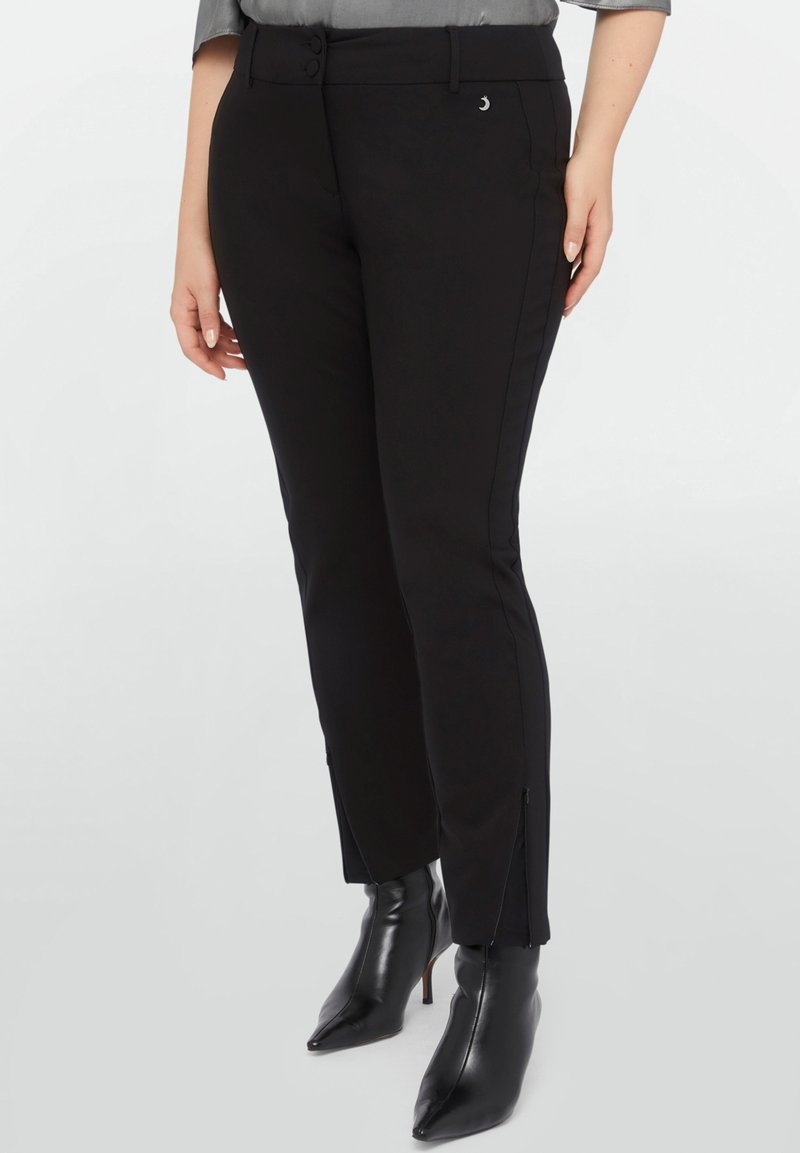 Pantalons noirs ajustés avec des zips sur les côtés. Fabriqués en tissu lisse, présentant une coupe près du corps et un léger éclat. Accent en métal argenté.