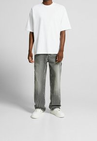 T-shirt bianco oversize, pantaloni grigi a righe con tasche e sneakers bianche. Il tessuto sembra morbido con una vestibilità rilassata e righe verticali.