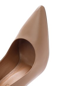 Chaussure à talons hauts en cuir beige, avec un bout pointu et une découpe latérale ouverte, présentant une texture lisse et un design minimaliste.