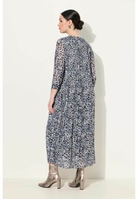 Sininen ja harmaa leopardi-kuvioinen maksimaalinen mekko, jossa on kolme neljännesosa hihaa ja pleatettua yksityiskohtaa, yhdistettynä metallisiin nilkkasaappaisiin.