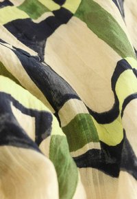 Mustriline kangas, kus on suured abstraktsed kujundid rohelises, mustas ja kooretoonides. Kerge, tekstuuriga materjal, mis langeb pehmelt.