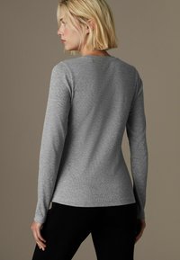 T-shirt gris à manches longues en tissu doux, avec un design ajusté et un col rond. Texture lisse avec de subtils détails de couture.