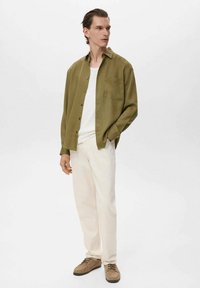 Olive green button-up shirt over a white t-shirt, paired with cream pants and brown suede shoes. Includes a chest pocket and relaxed fit.