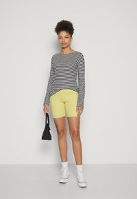 Majica s dugim rukavima u crno-bijele pruge, uparena s uskim žutim kratkim hlačama. Dodaci uključuju crnu torbu i bijele tenisice.