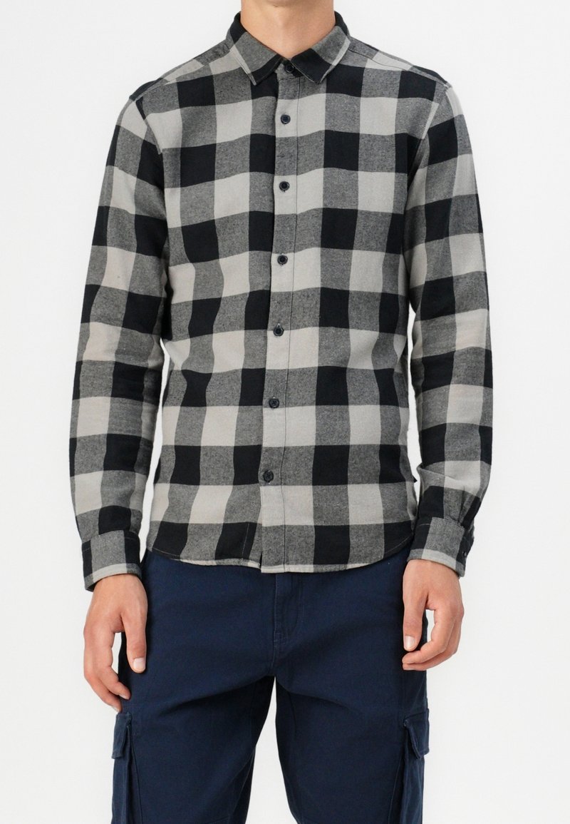 Camisa de manga larga a cuadros en negro y gris con una botonadura, collar en punta y tejido estampado; combinada con pantalones azul marino.