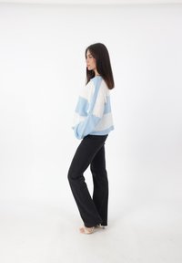Blau-weiß gestreifter, übergroßer Pullover mit lockerer Passform, kombiniert mit schwarzen Schlagjeans und beigen High Heels. Angenehme, weiche Textur.