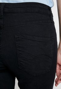 Černé džíny z denimu s hladkou texturou a zakřiveným designem zadní kapsy. Vysoký pas se standardním zipem a knoflíkovým zapínáním.