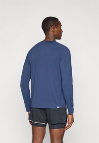 Long-sleeve navy athletic shirt with raglan sleeves, smooth texture, and contrasting seam detail, paired with black athletic shorts.