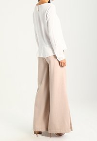 Top bianco a maniche lunghe con dettaglio a chiave sul retro, abbinato a pantaloni a gamba larga di un beige chiaro, realizzati in tessuto morbido.